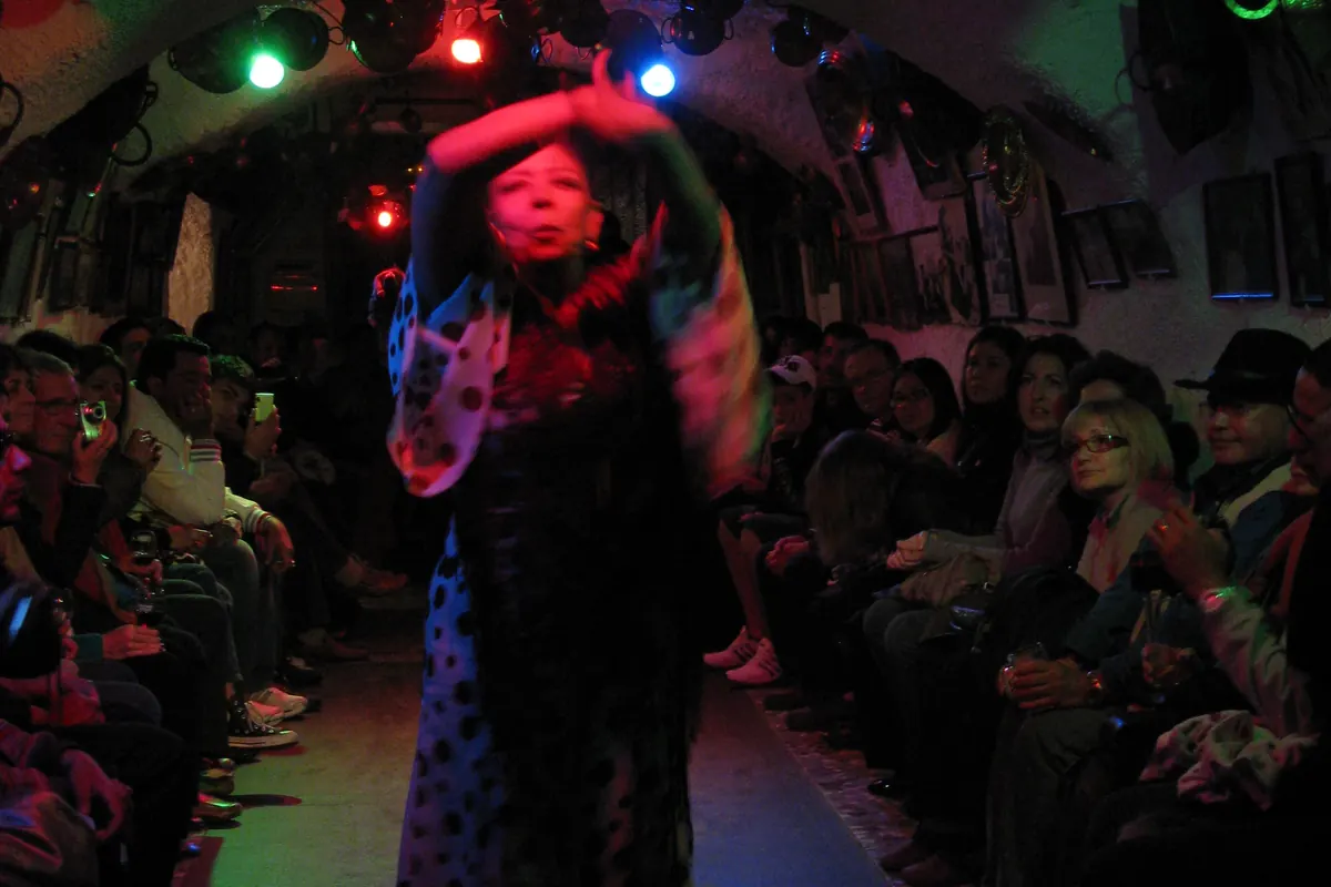A flamenco dancer in a polka-dot dress performing in a whitewashed Sacromonte cave, with guests seated along both walls