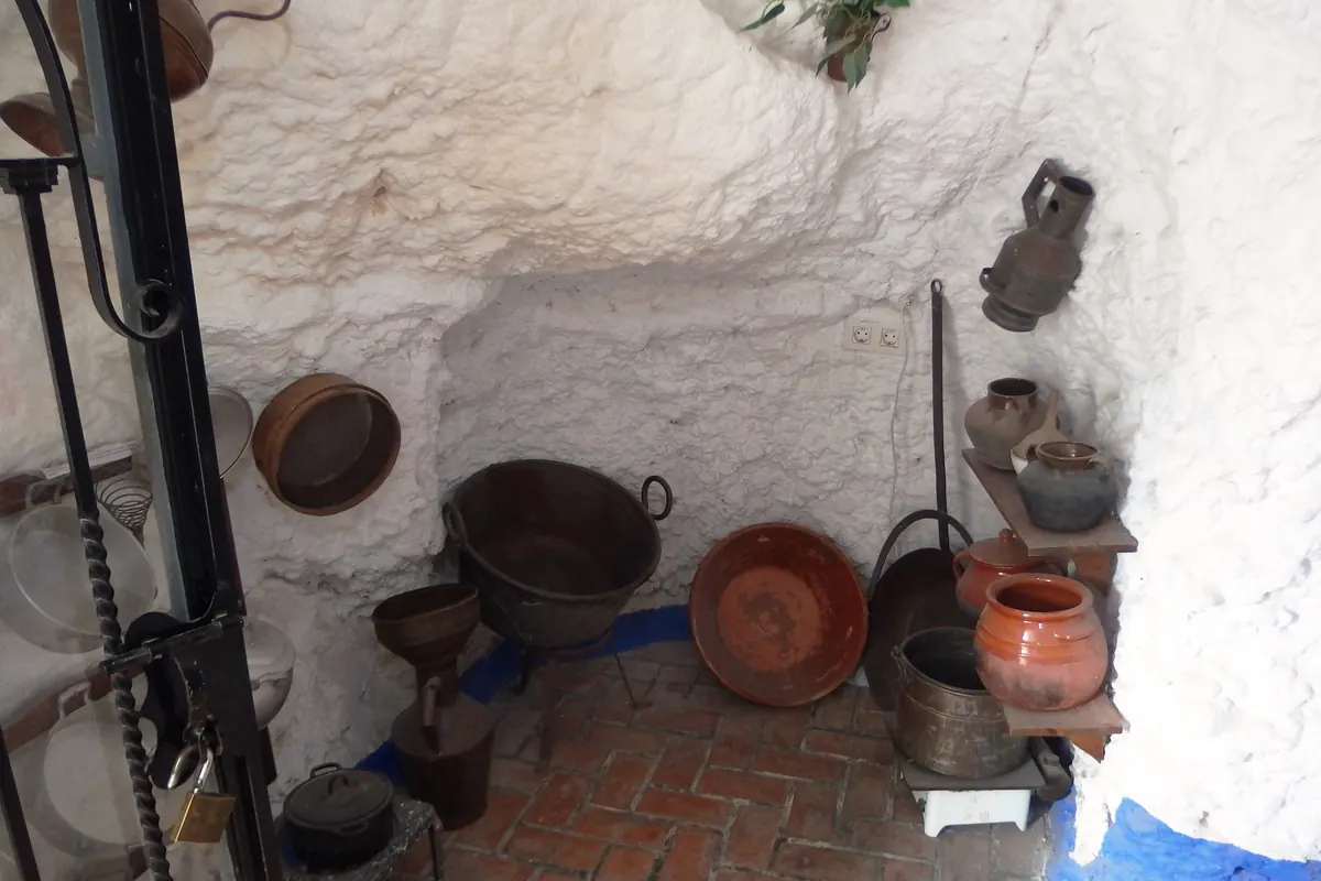 A whitewashed cave room with copper pots and clay jars at the Sacromonte caves museum