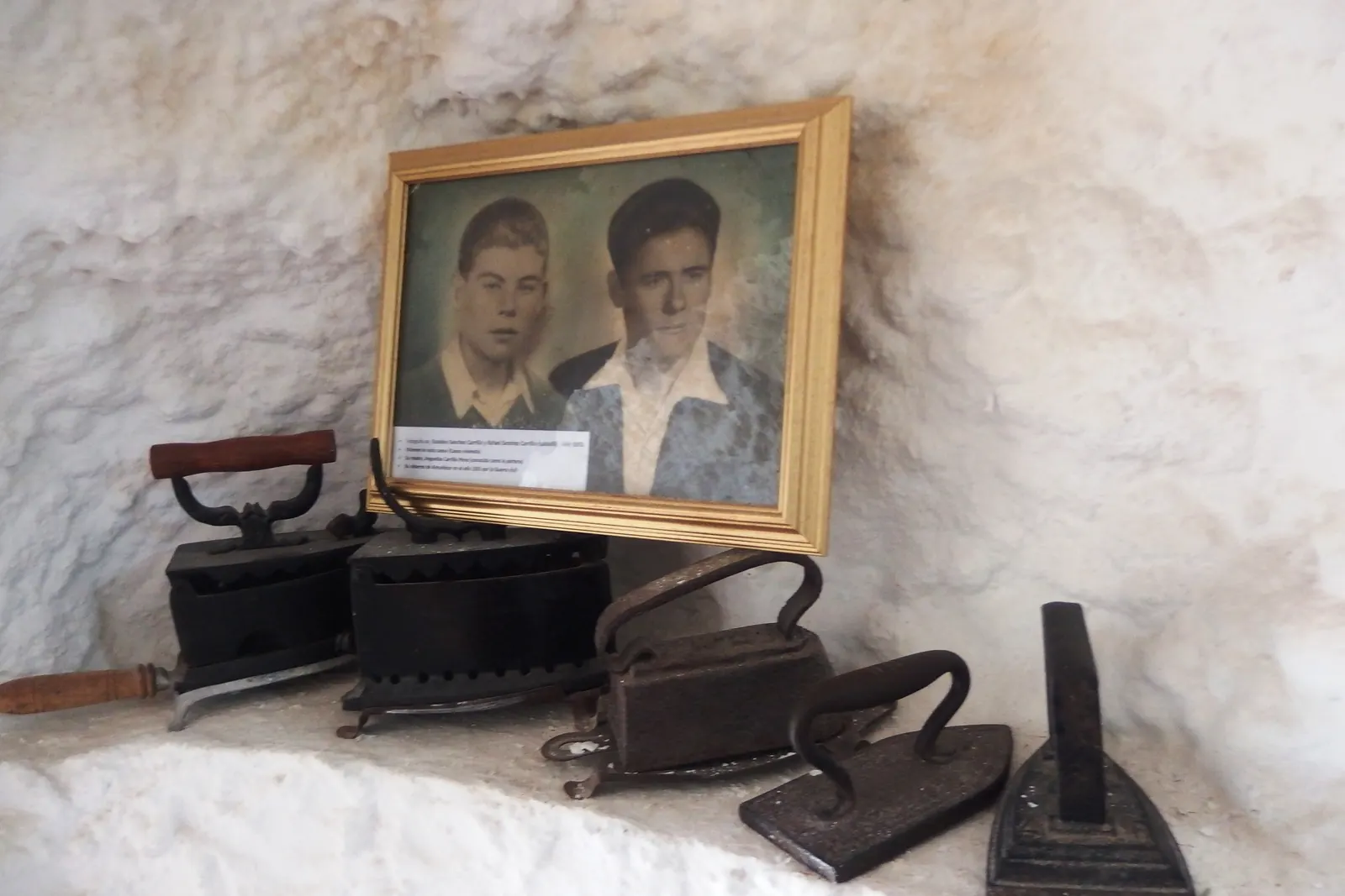 Old flat irons and a framed photograph of two young men on a whitewashed cave shelf in a Sacromonte museum